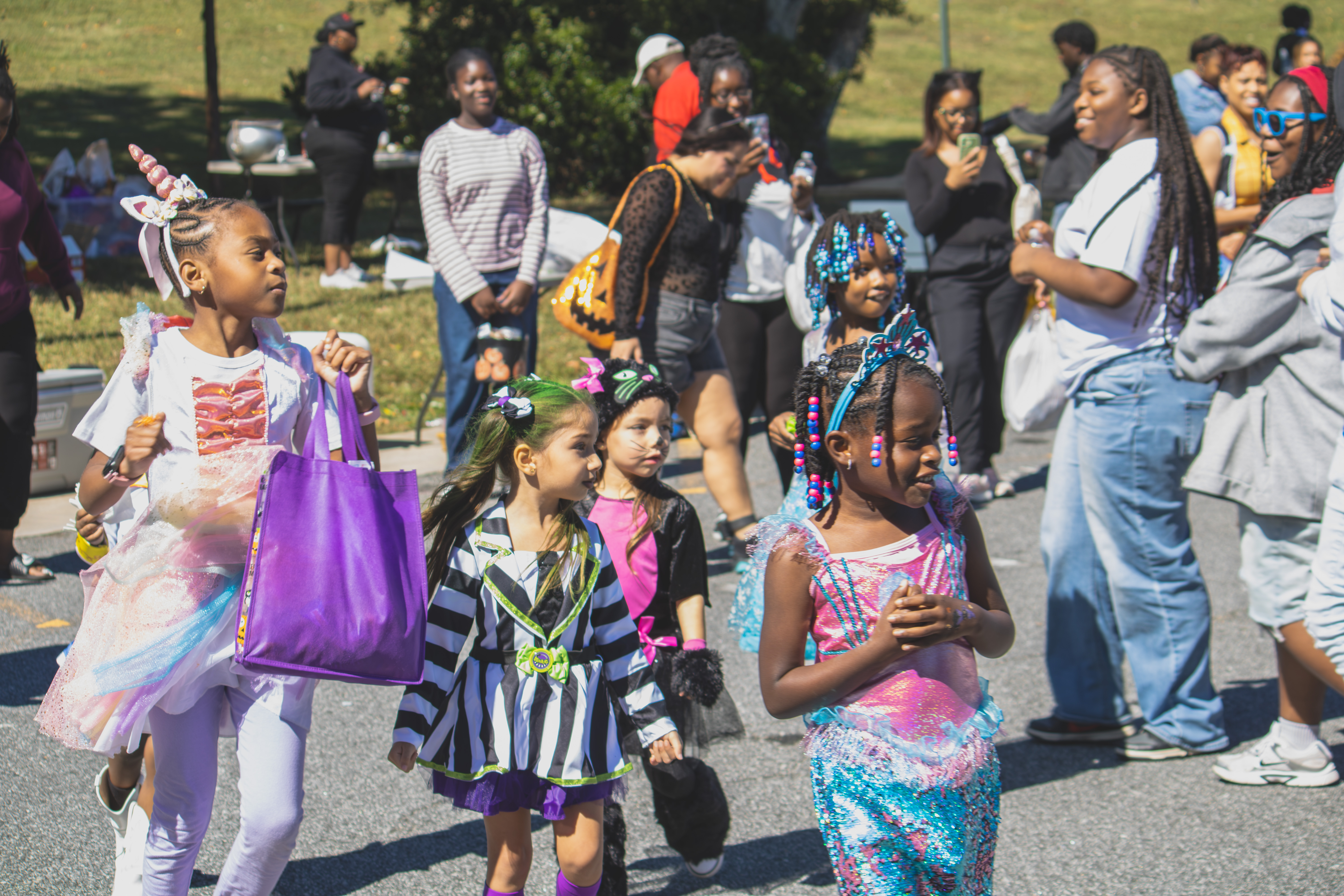 Children in unicorn, striped, cat, and mermaid costumes gather with families at Trunk or Treat.